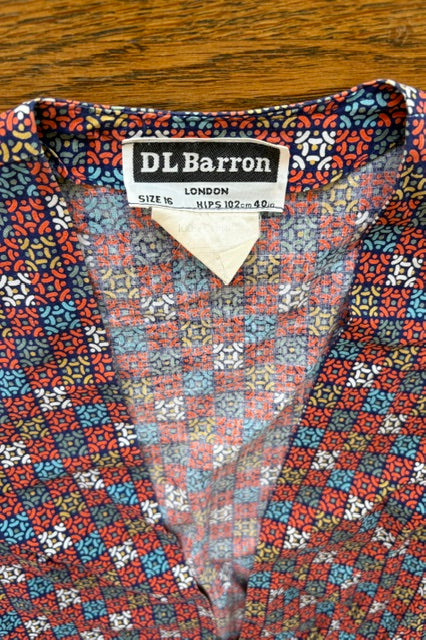 Close-up of a DL Barron patterned shirt with a visible neck label, showing a multicolor floral and geometric print on a wooden surface.