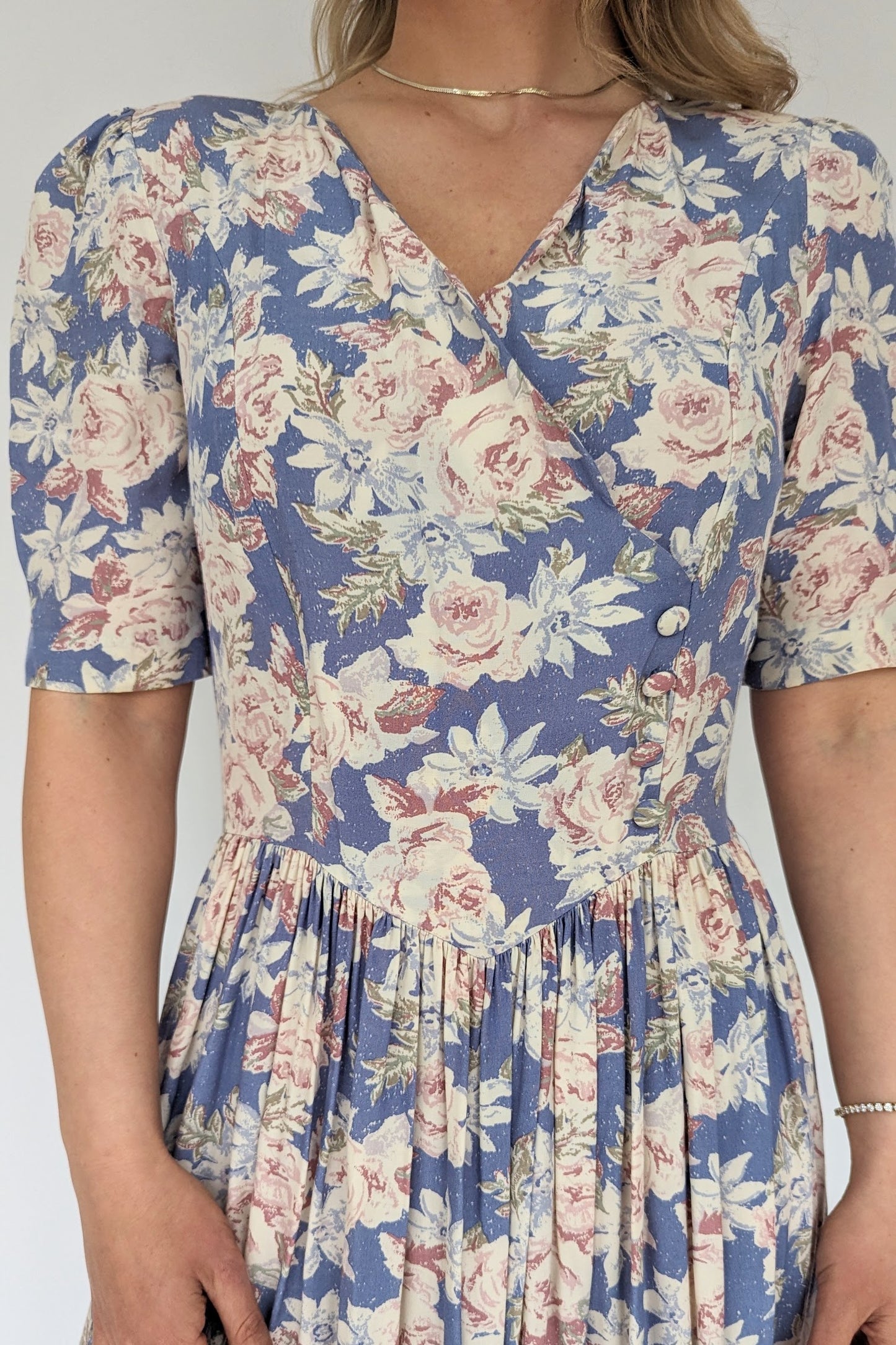 front view of vintage laura ashley long floral dress in light blues and pinks with puff sleeve and gathered v waist with side buttons to the front 