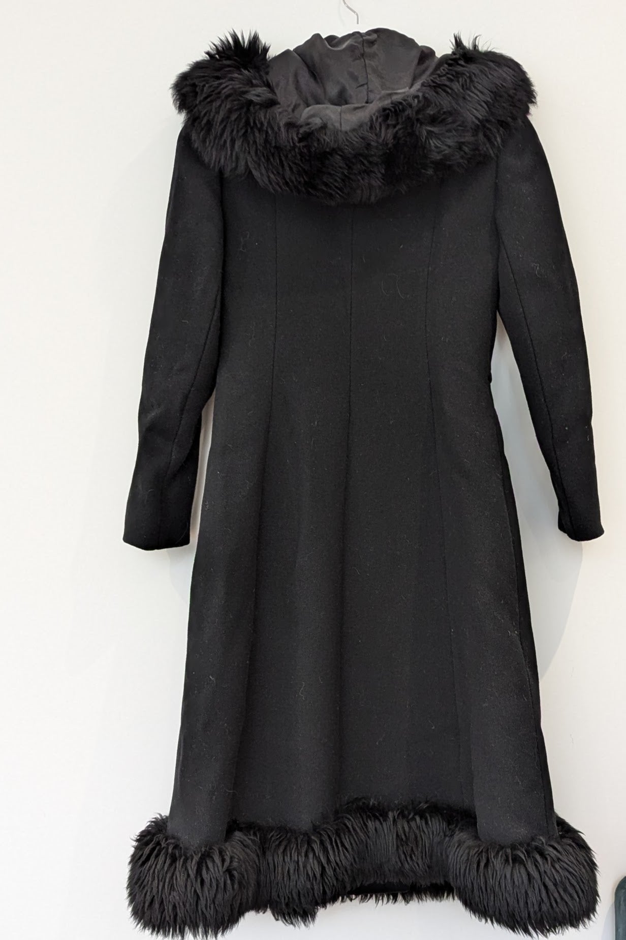 back of vintage hooded black long winter coat with fur trim and side buckle on hanger