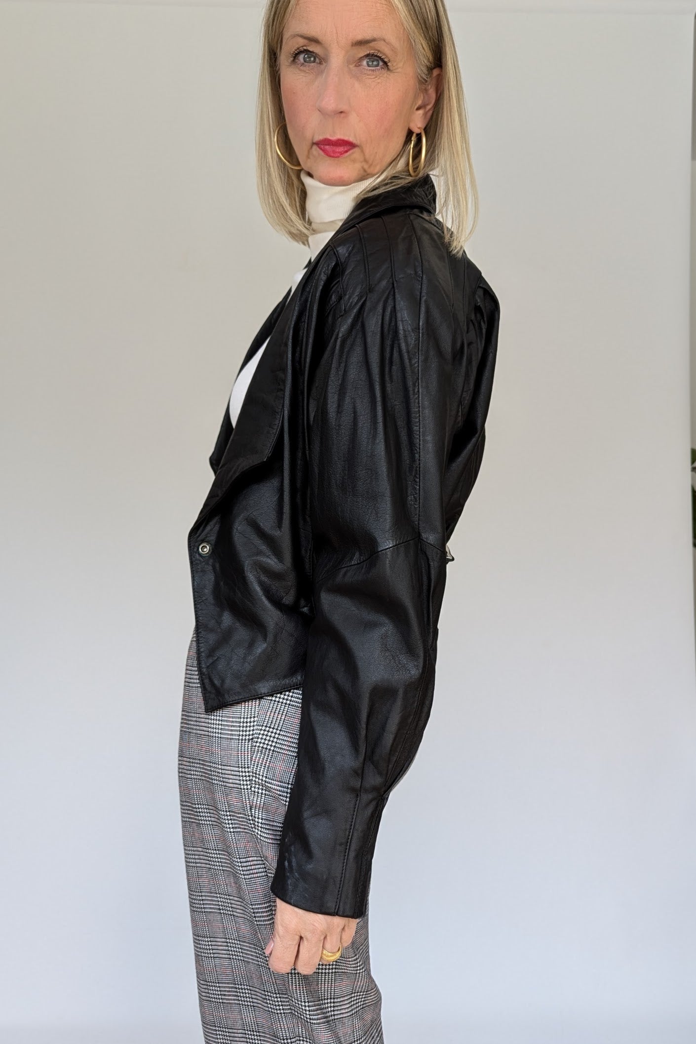 side of short black leather 80s jacket with buckle to the back