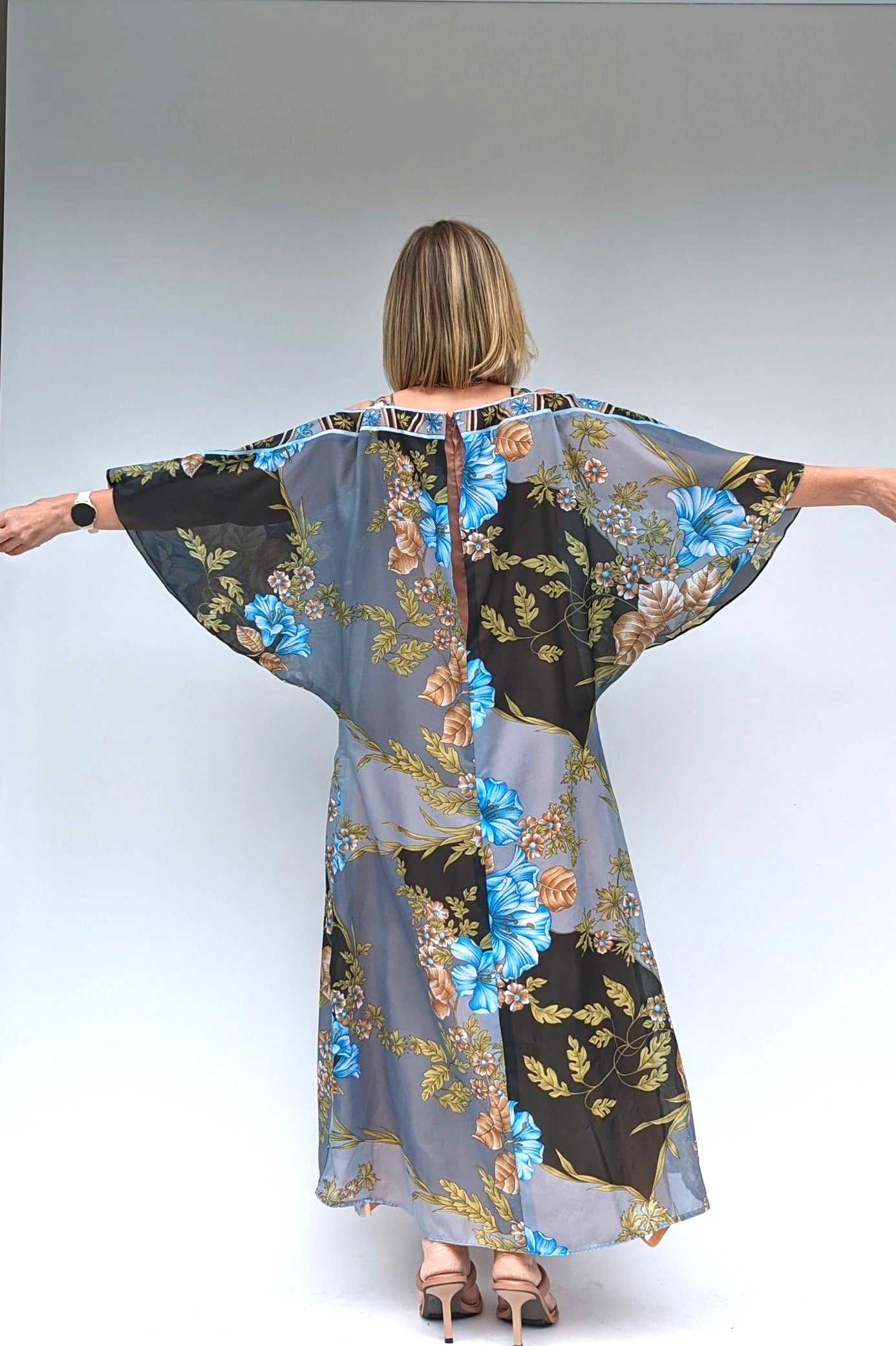 back of Long bat sleeved vintage floral kaftan in grey, black, blue and brown with a sheer overlay and a dusky peach lining showing bat sleevess